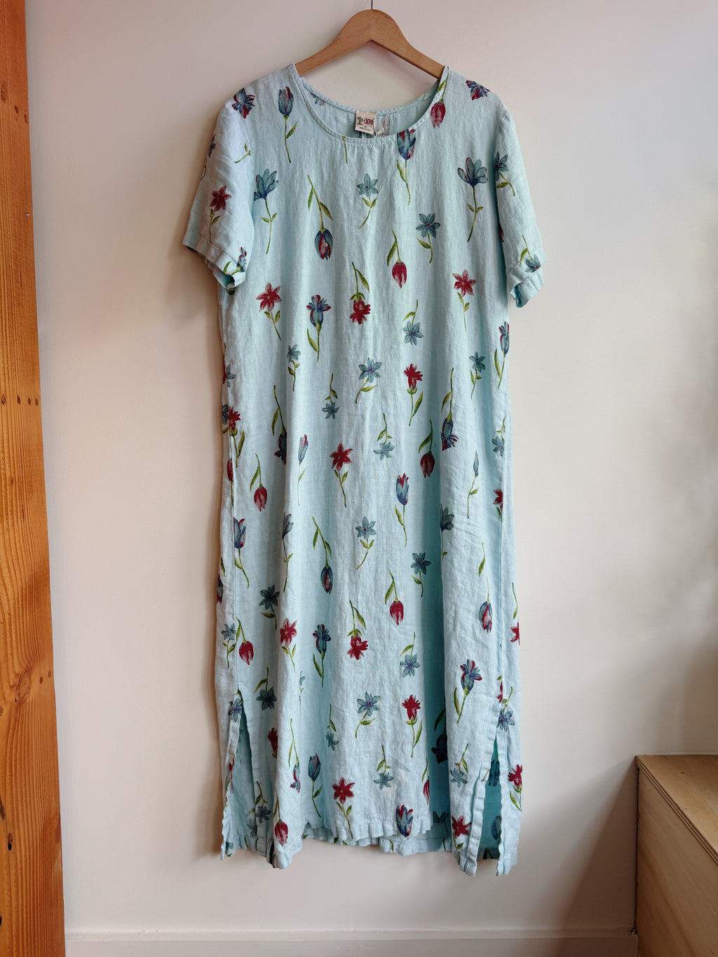 Floral dress hanging on a wooden hanger against a white wall.