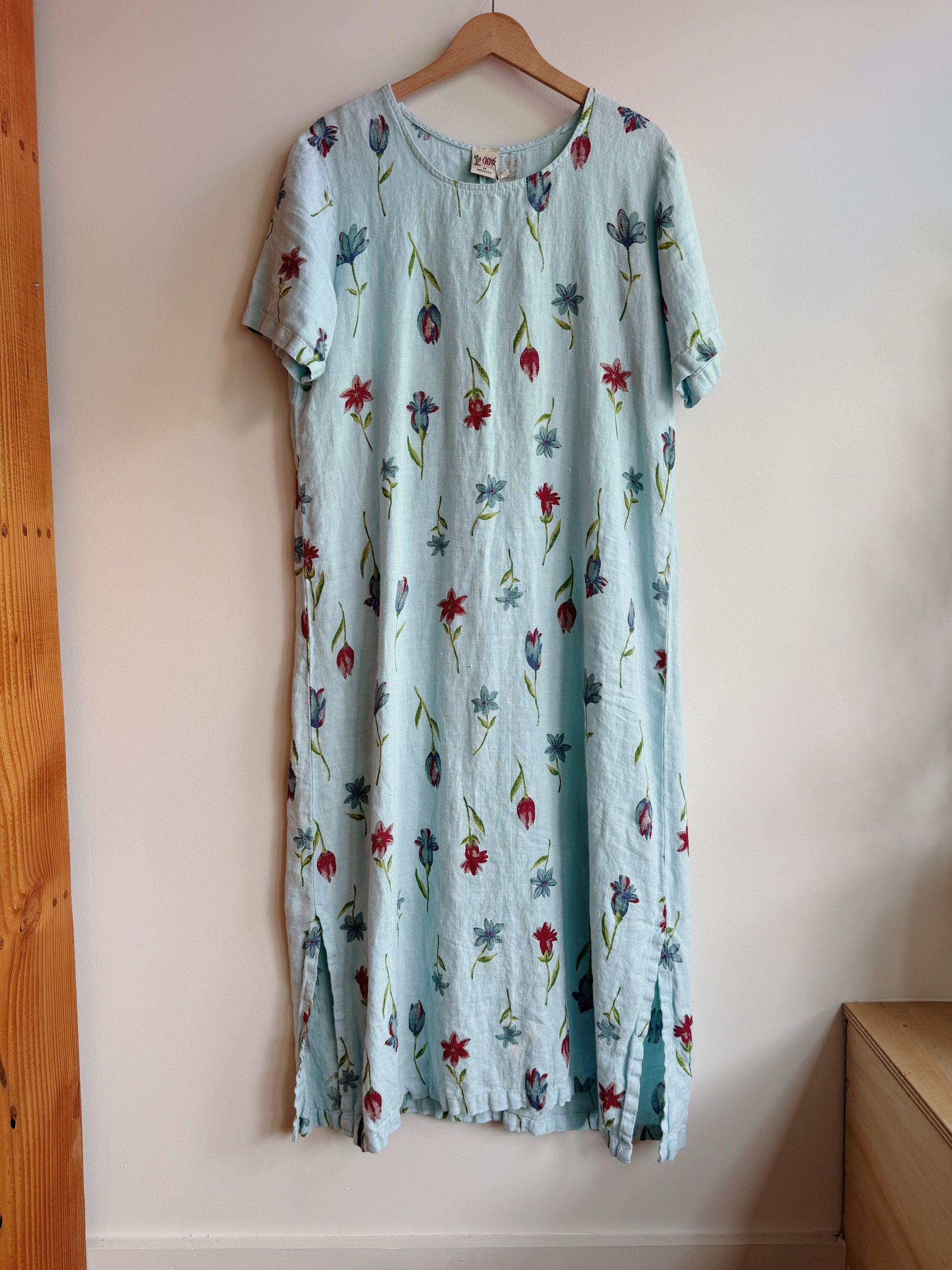 Floral dress hanging on a wooden hanger against a white wall.